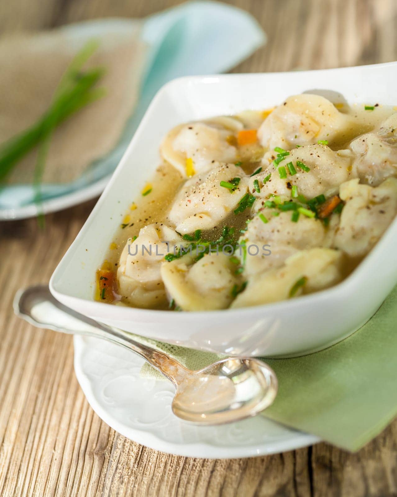 Bowl with Russian Pelmeni Italian tortellini with broth and parsley close-up on a wooden table