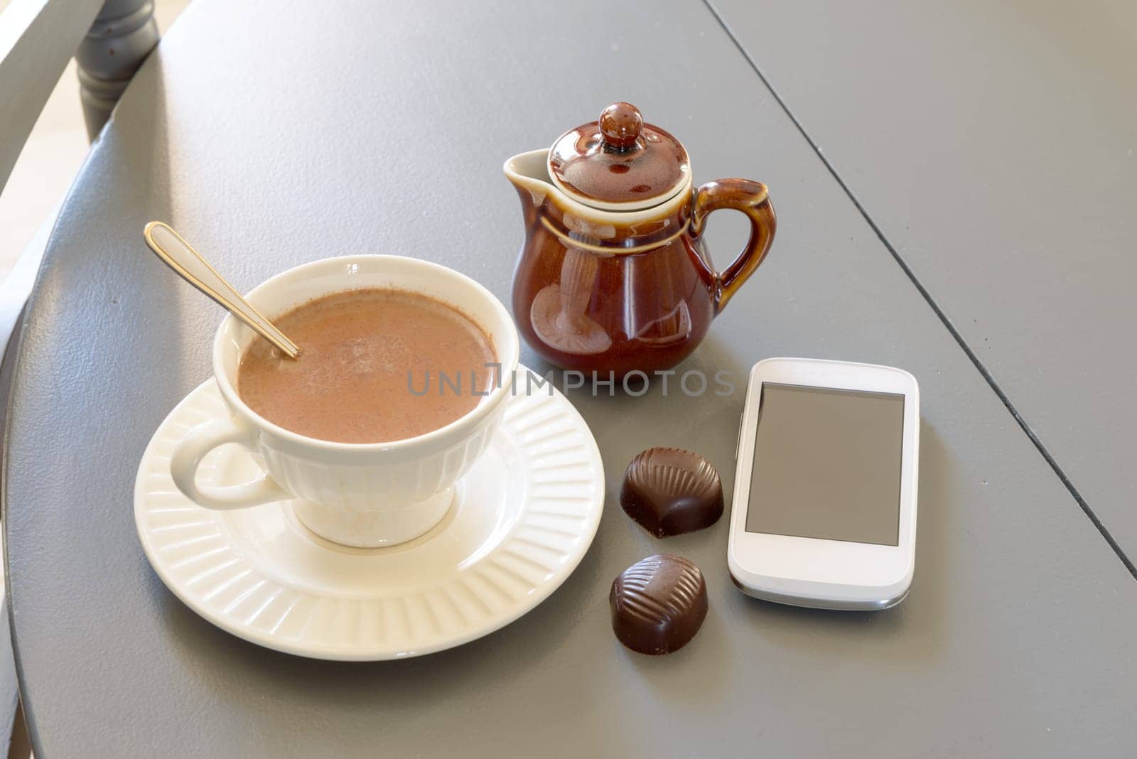 cup of hot chocolate with a phone on a grey table