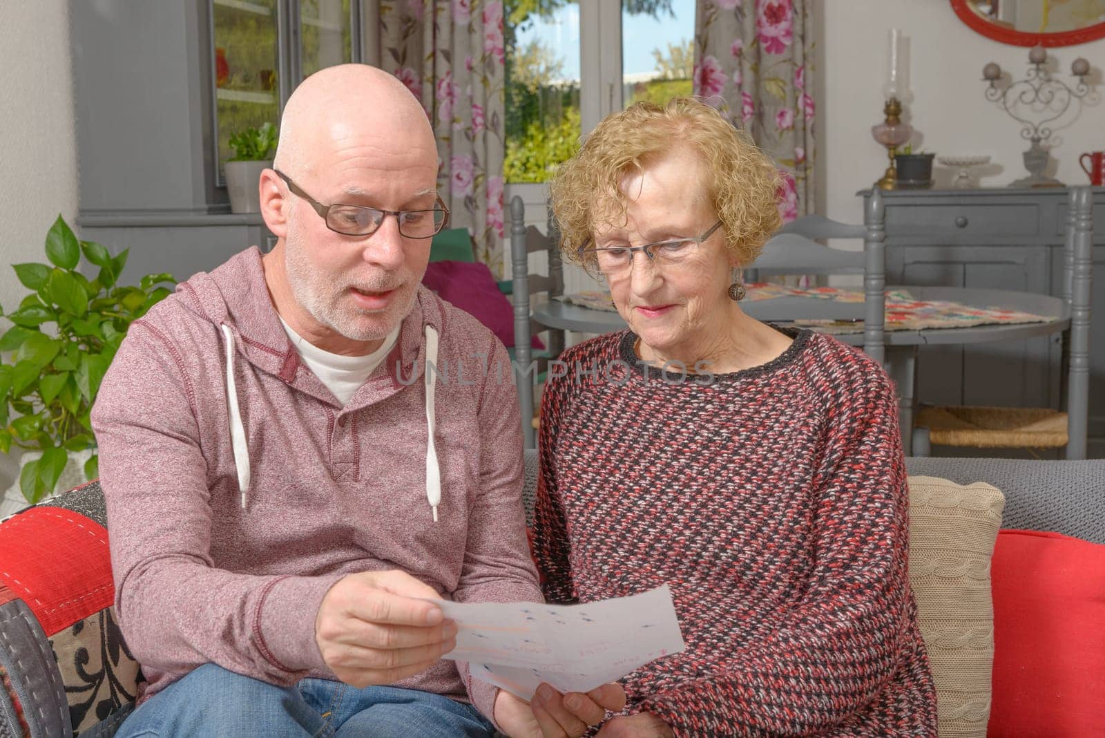 a mother and her adult son looking paper on a sofa