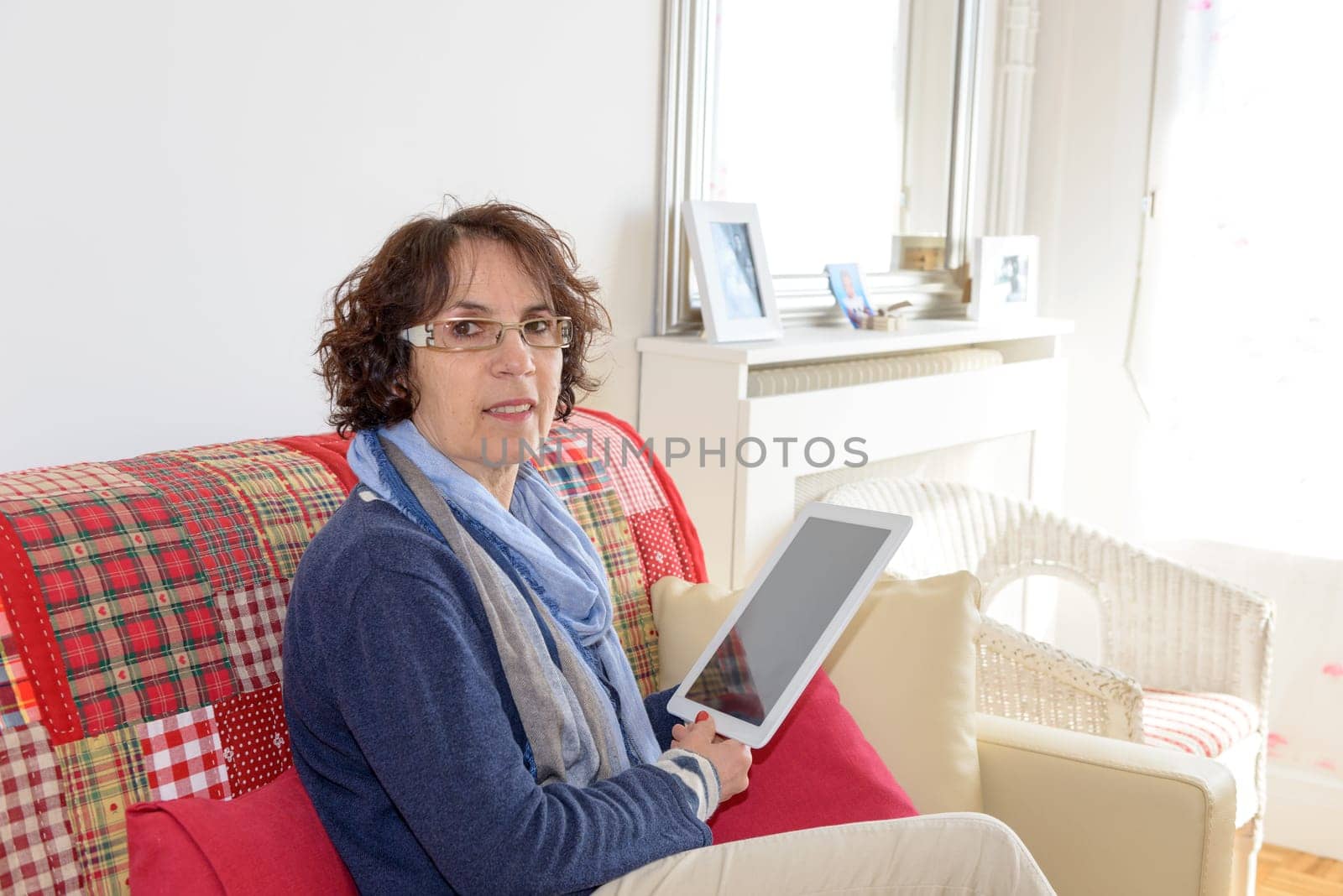 a middle aged woman smiling with a digital tablet on her sofa