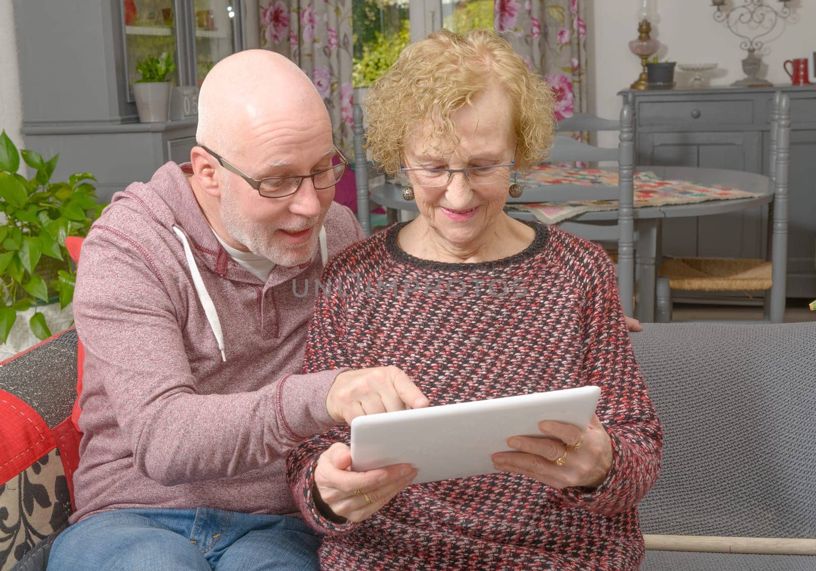 a mother and her adult son looking at a digital tablet on a sofa