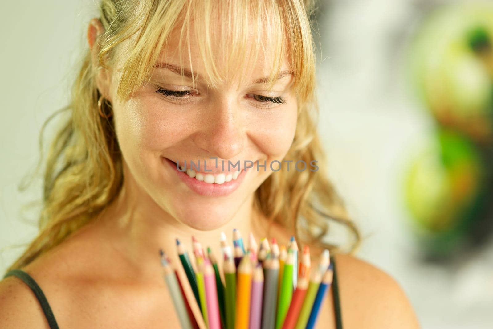 Portrait of young woman holding bunch of colorful pencils at camera and smiling