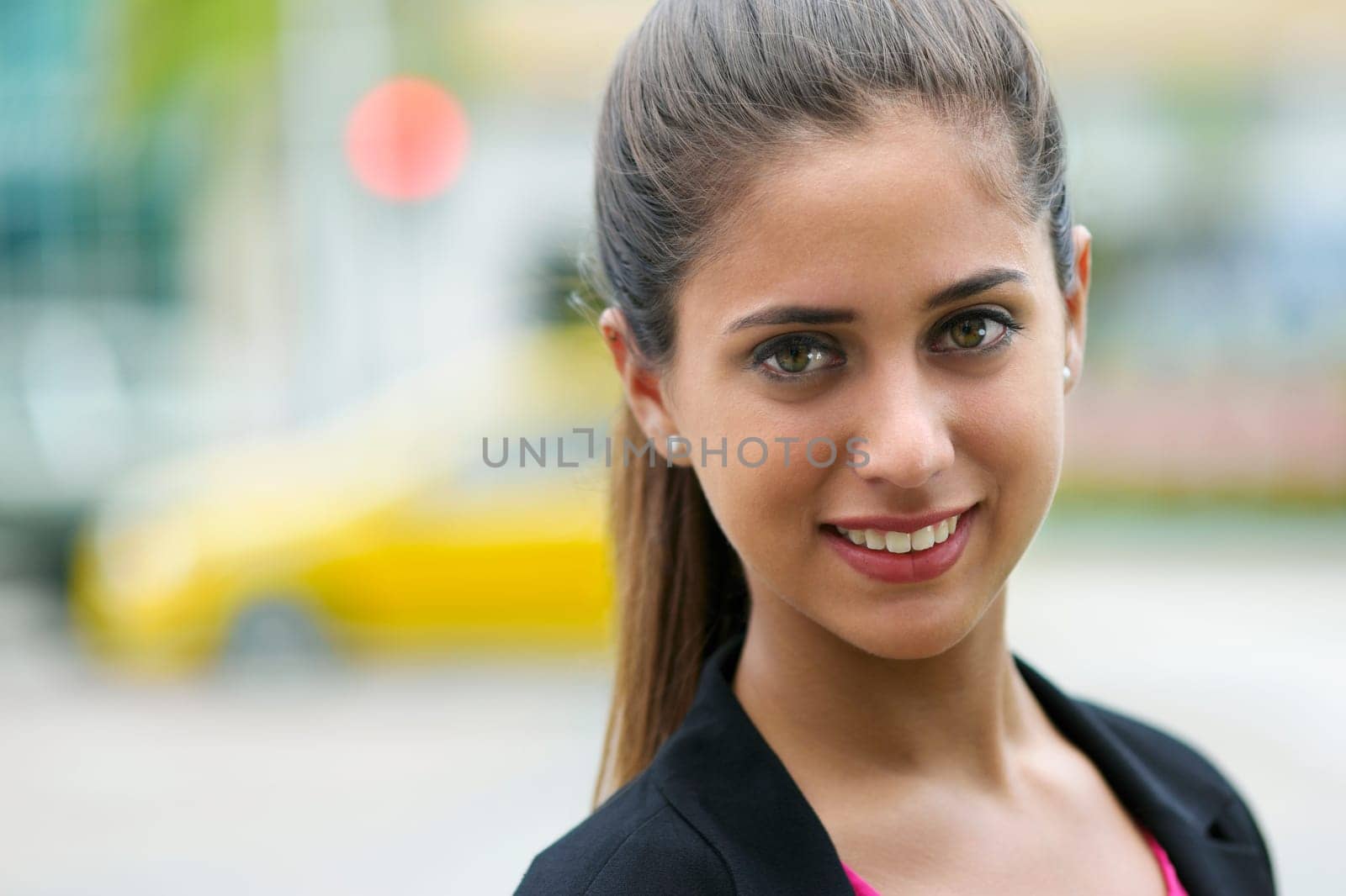 Portrait of young confident hispanic business person looking at camera and smiling in the street with cars passing behind