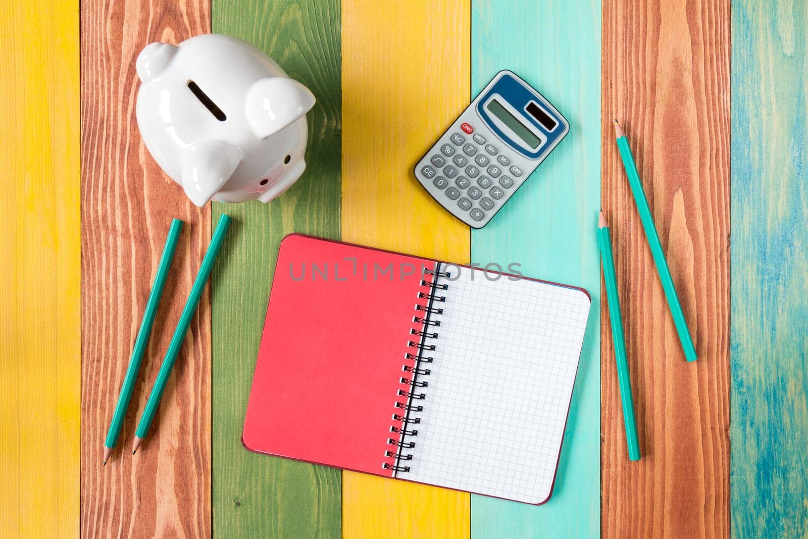 Calculator,open notebook,piggy bank and four pencils.Top view.