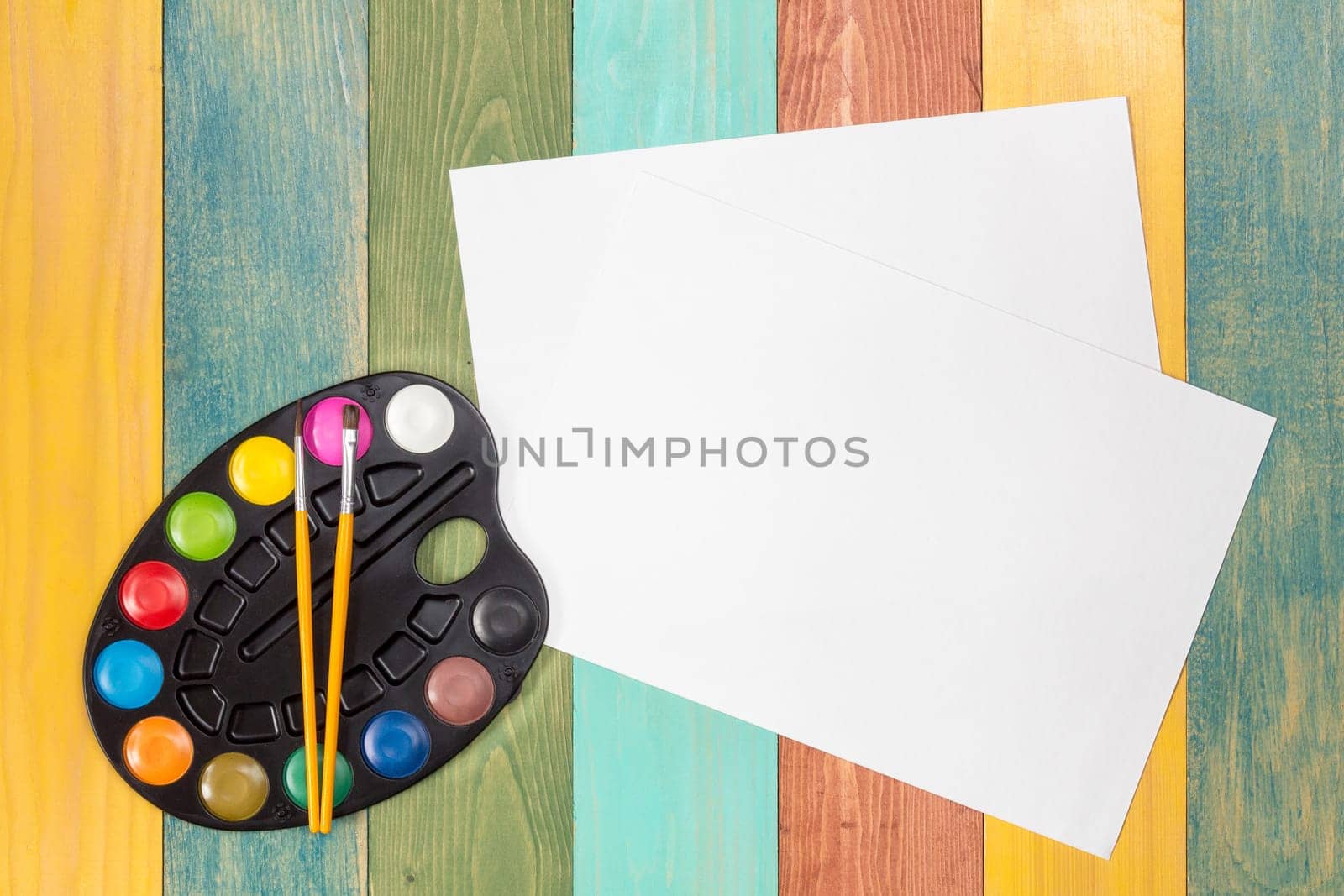 Watercolor paint and white paper sheet on color wooden background. Top view