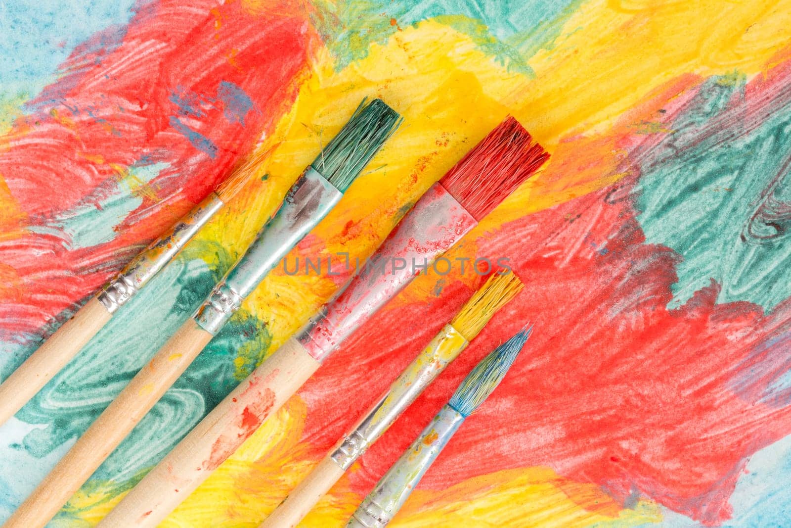 Five dirty watercolor brushes on abstract colorful painting
