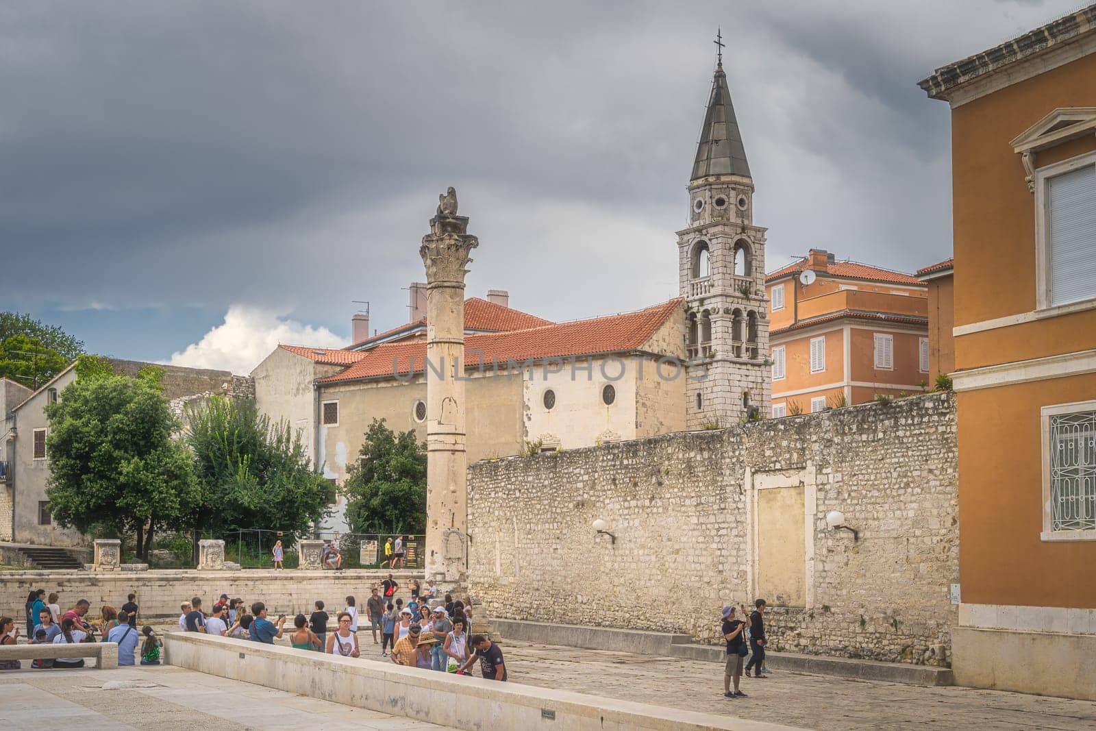 Zadar, Croatia, July 2019 Tourists admiring and photographing old Roman ruins, a column with sculpture and St. Donata Church, Pope John Paul II square