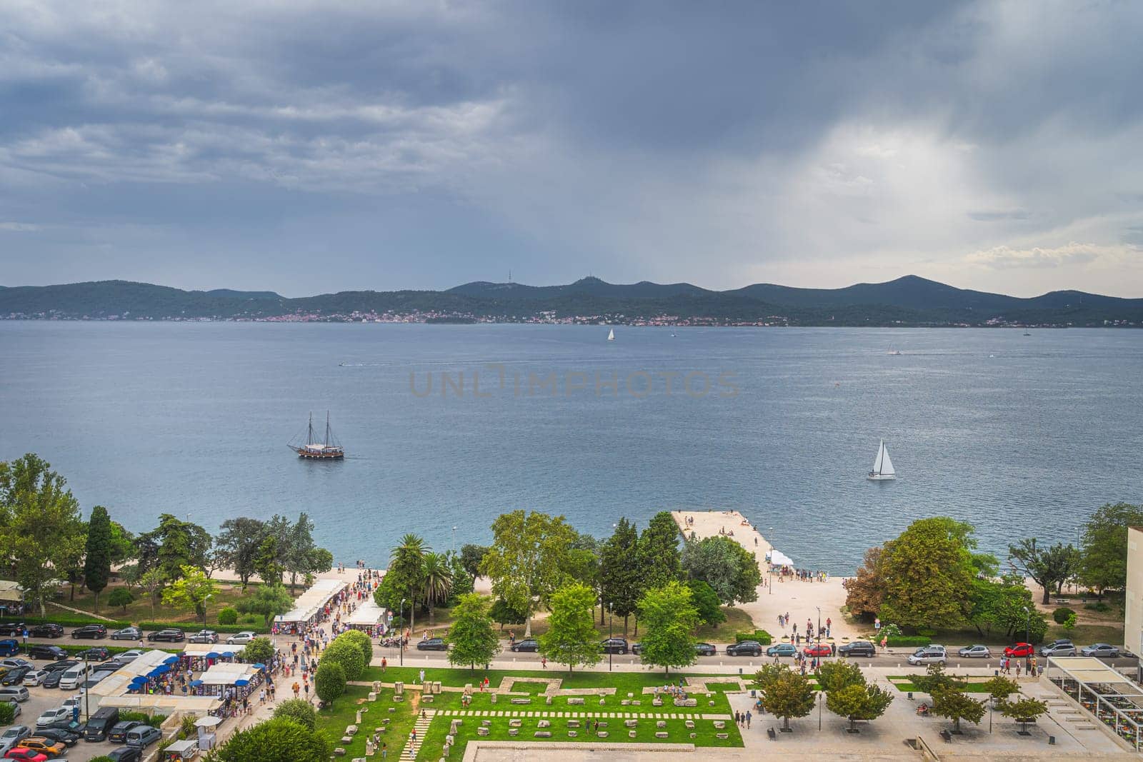Drone or aerial view on crowds of tourists visiting a market on the pier in old town district of Zadar with sailboats sailing on Adriatic Sea, Croatia