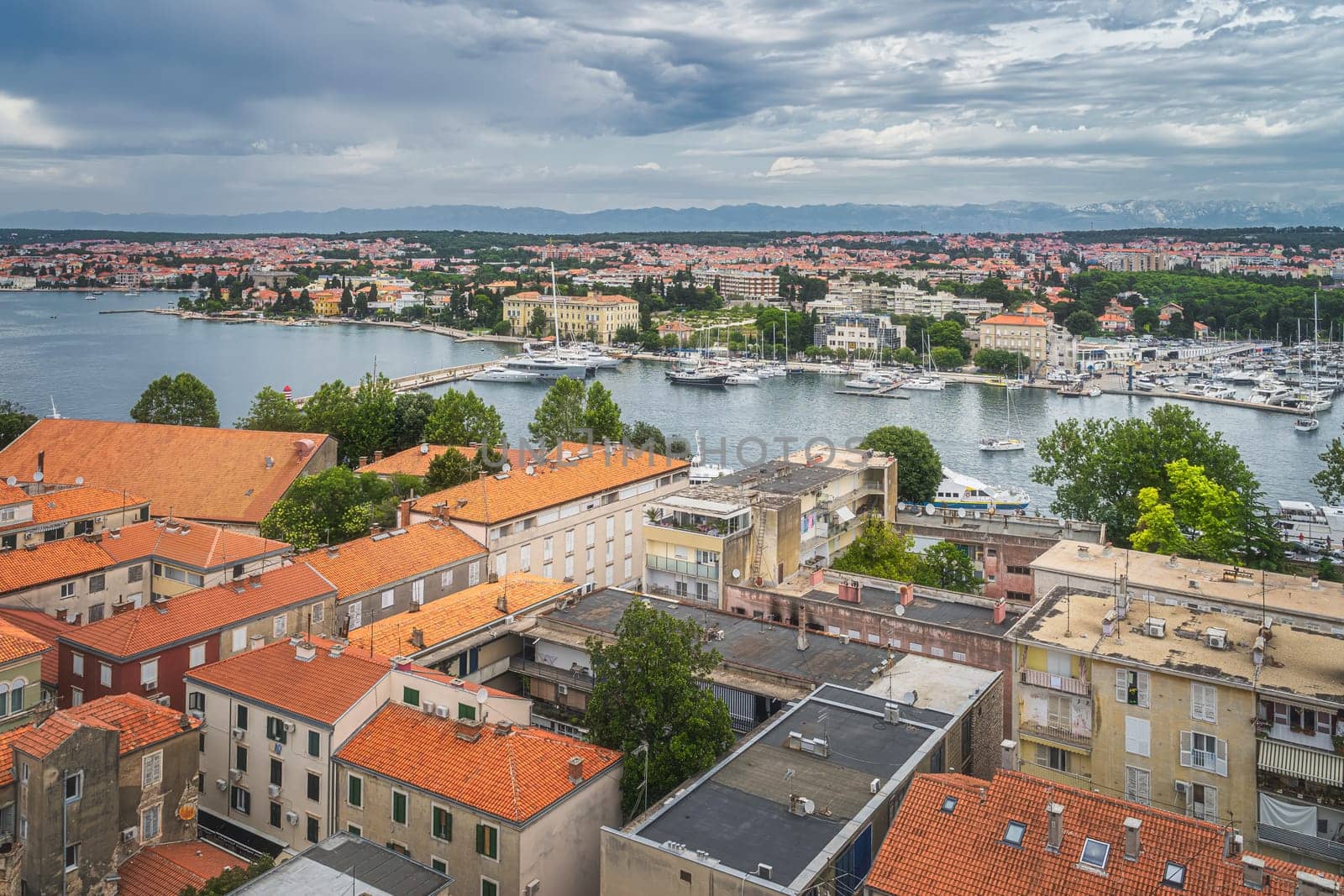 Drone or birds eye view on orange tiled roofs and cityscape of Zadar. Bay or marina with moored yachts and boats, Croatia