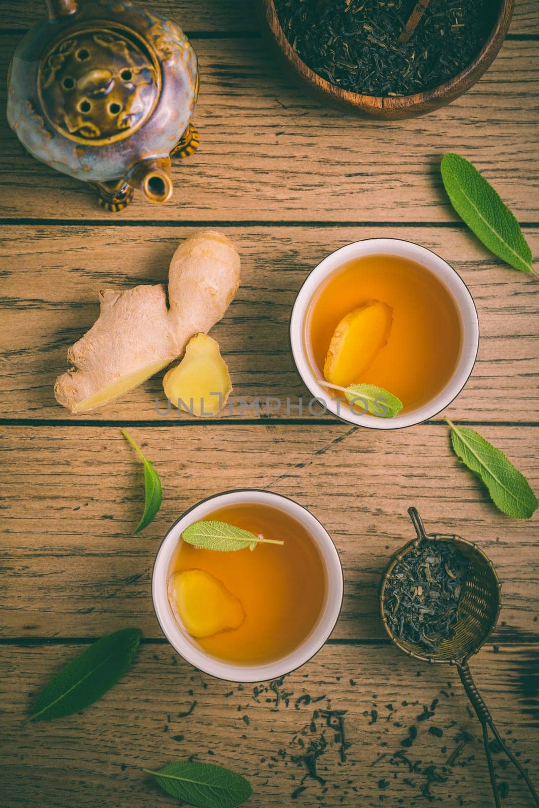 Ginger tea with sage leaves and dried black tea leaves on wooden background