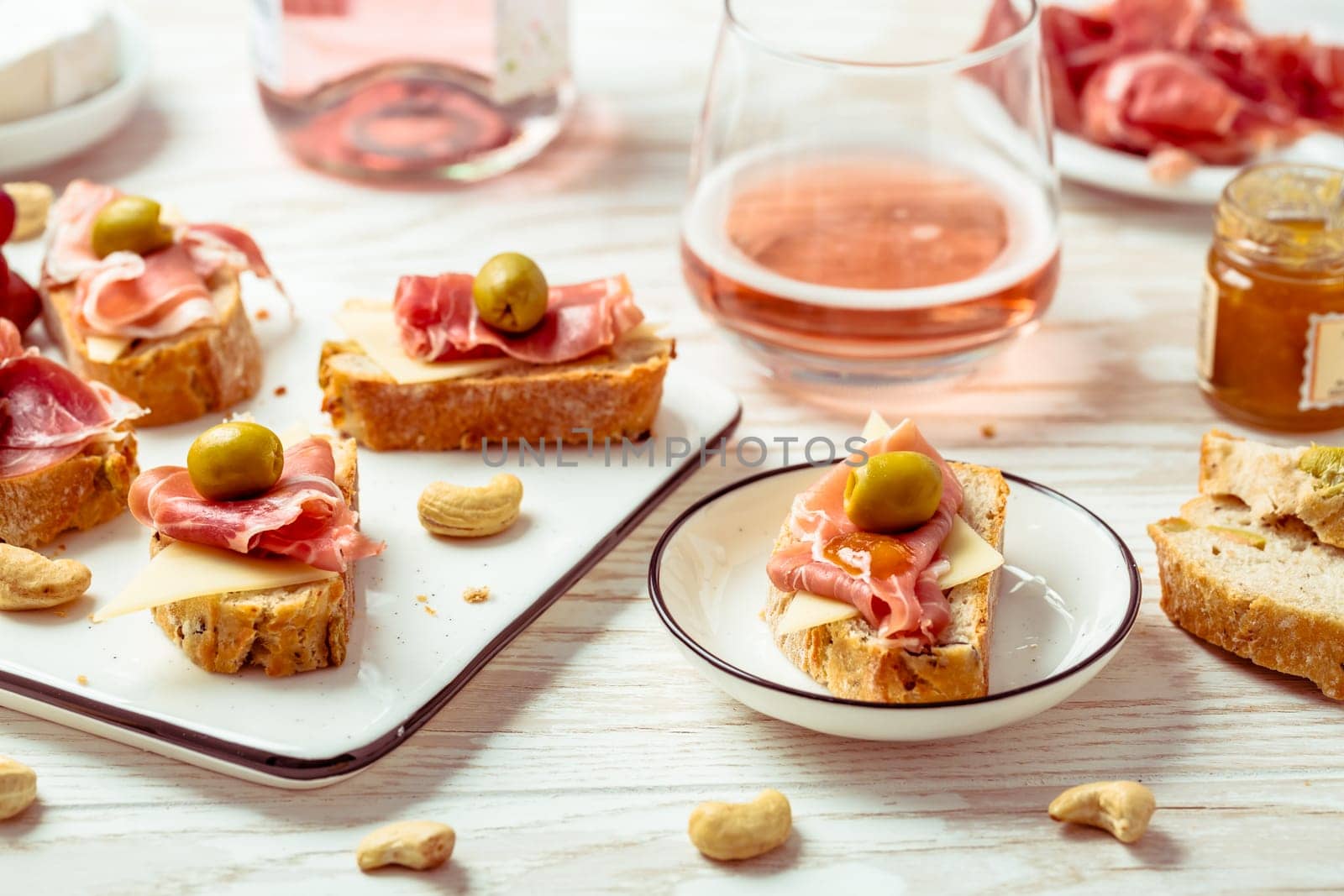 Appetizers and open sandwiches with Italian antipasti, camembert, Parma ham and rose wine on wooden table
