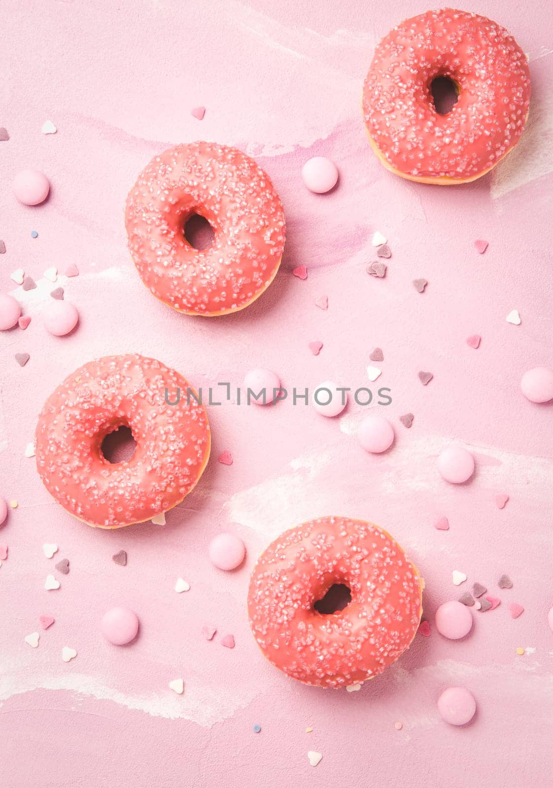 Donuts with pink icing and pink chocolate beans on pink background