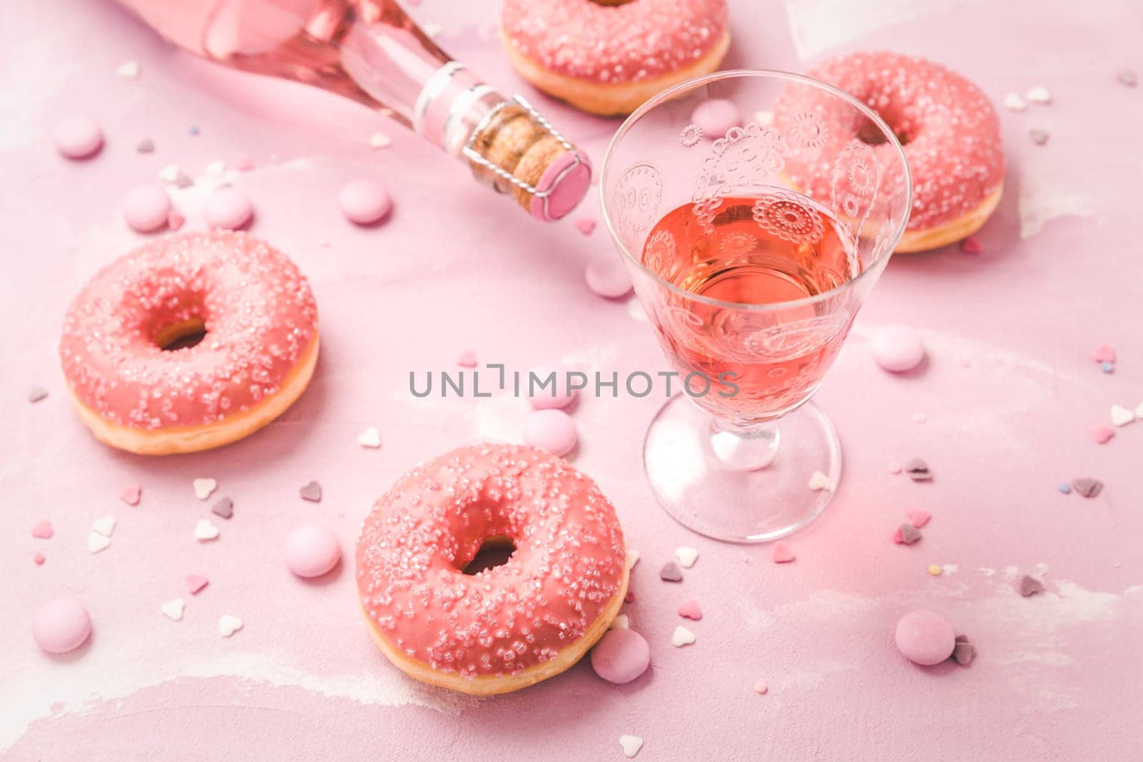 Rose wine or cocktail with pink donuts and pink chocolate beans on pink background