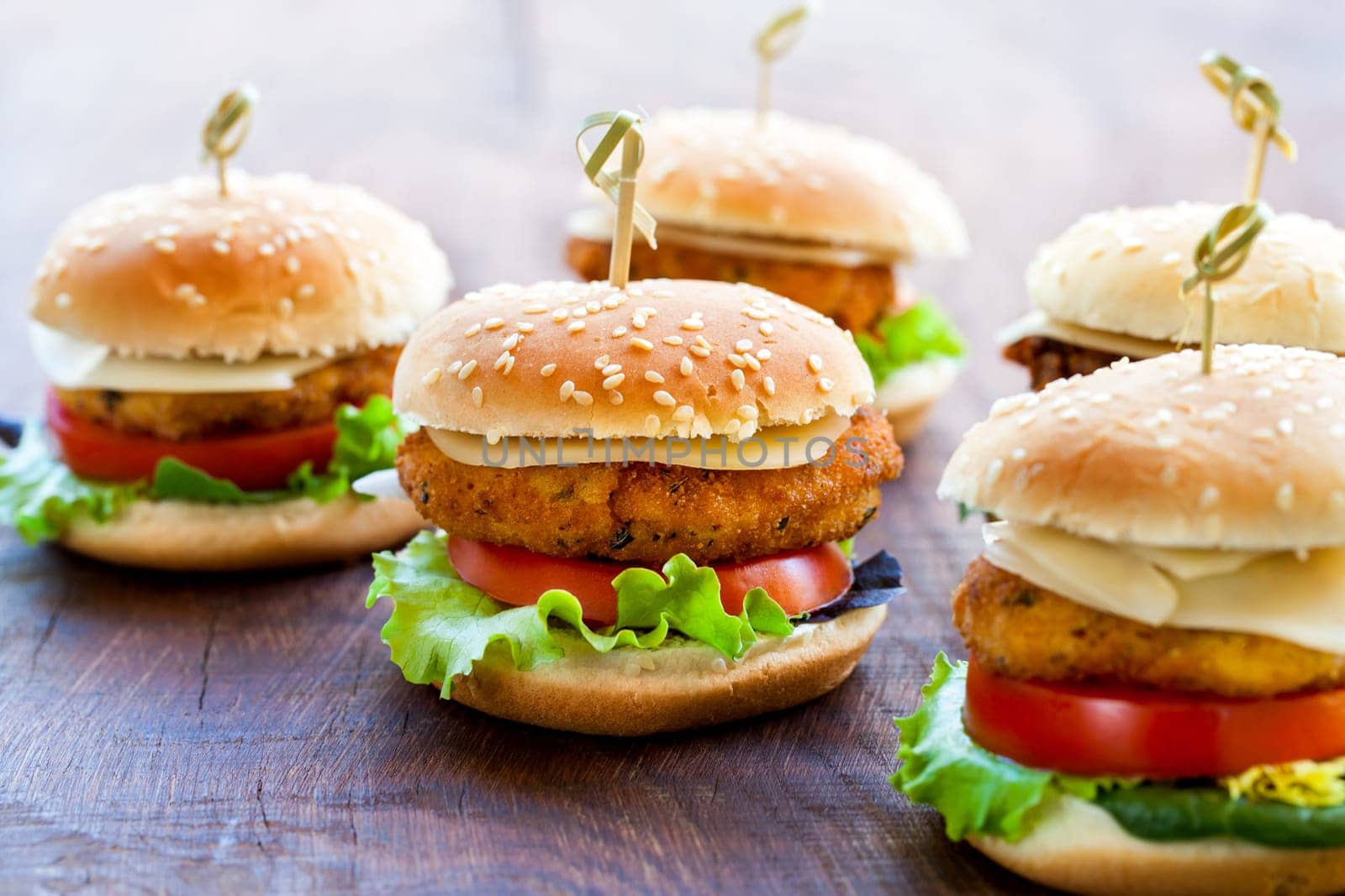 Macro close up of multiple appetizing mini chicken burgers on wooden surface.