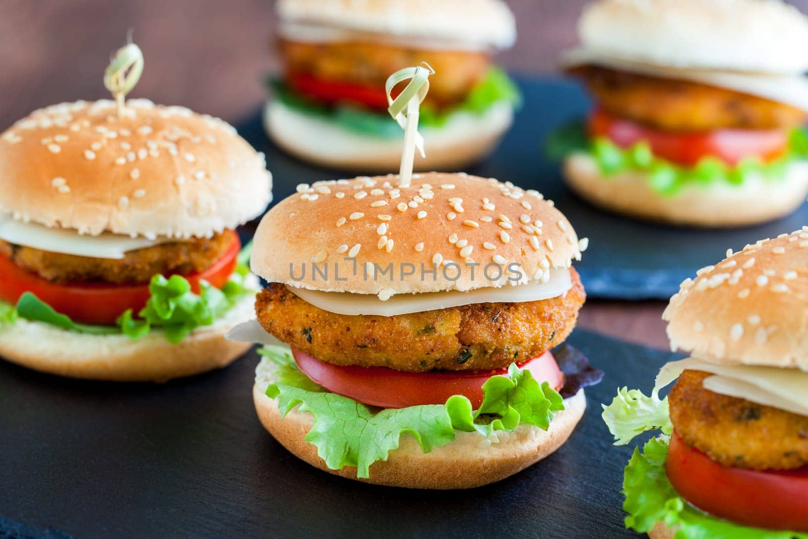 Extreme close up of multiple Appetizing mini chicken burgers. Small burgers in row for catering service.
