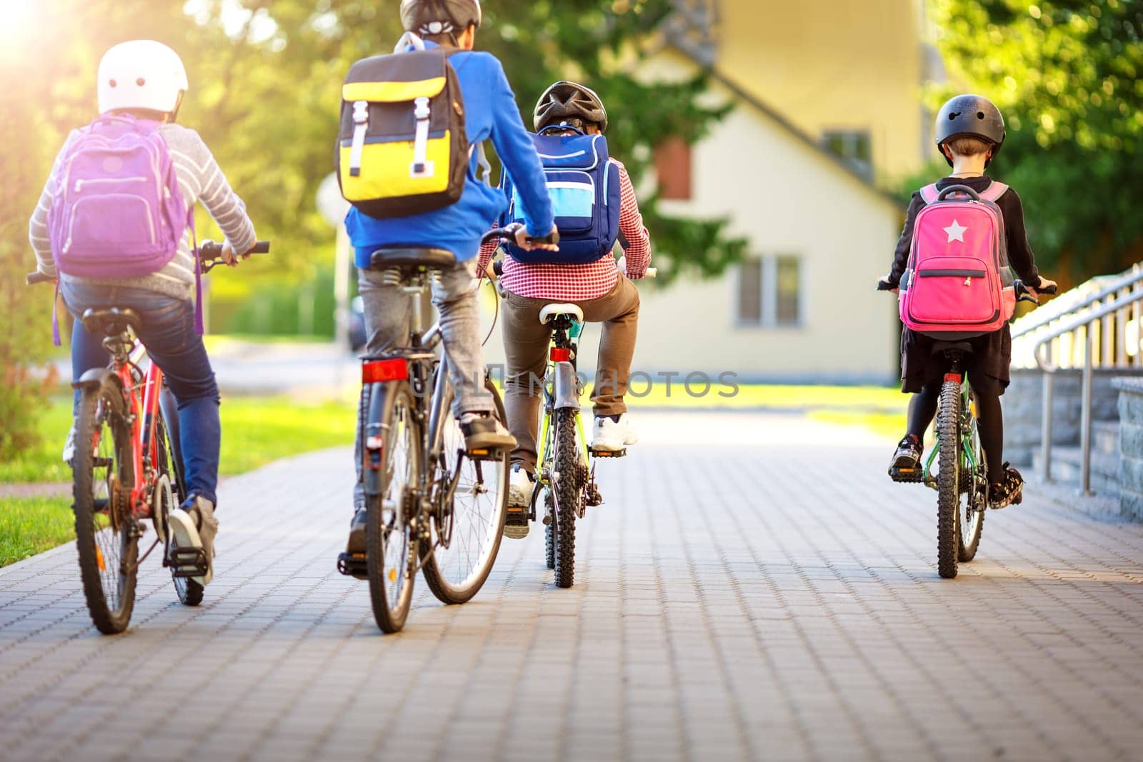 Children with rucksacks riding on bikes in the park near school. Pupils with backpacks outdoors
