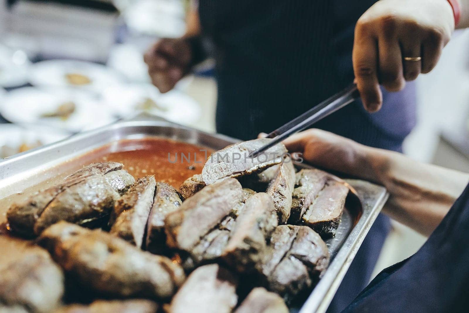 A baking tray with roasted meat. Take a piece of meat to taste.