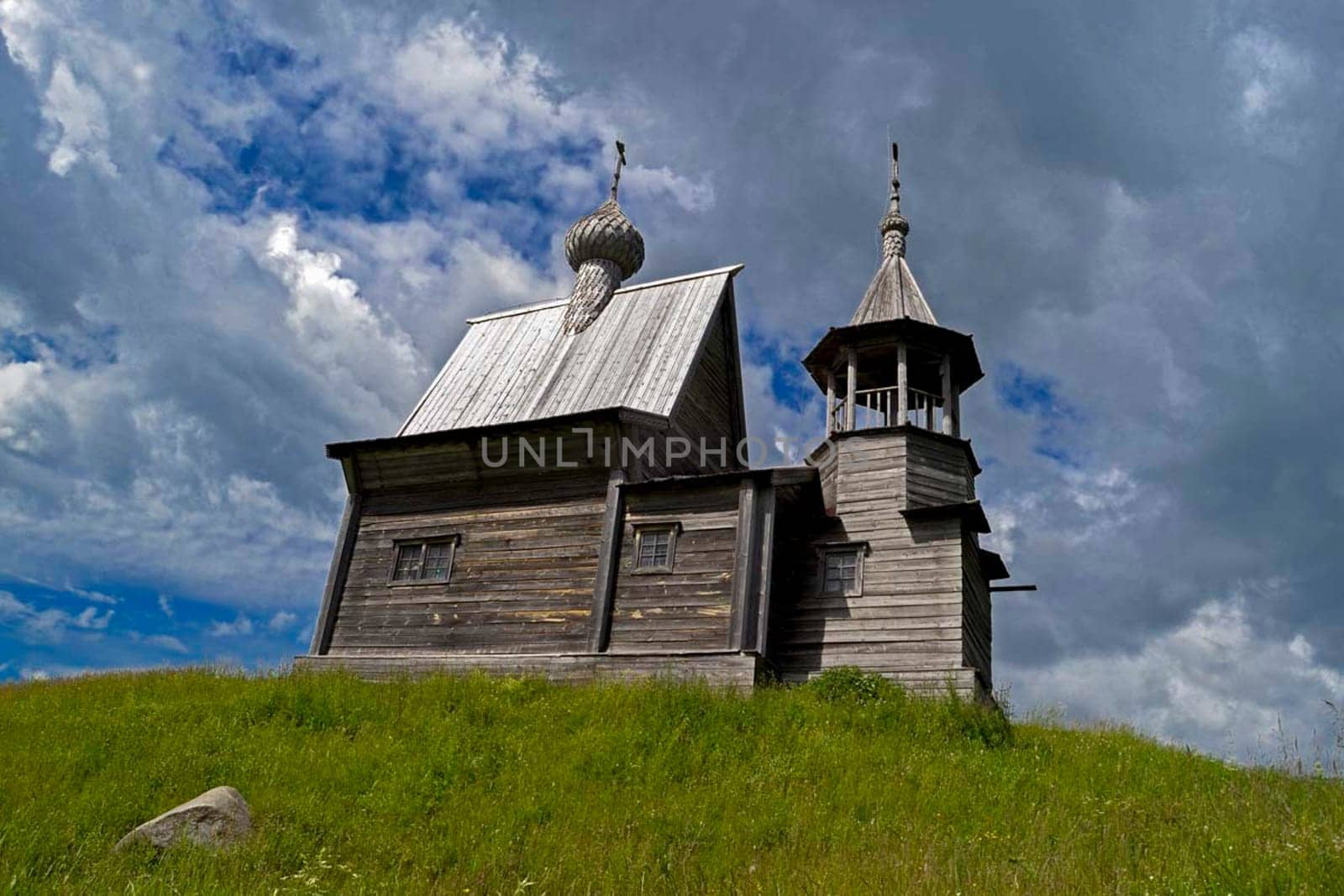 A wooden church on a green hill. Grass on the choir outside the church.