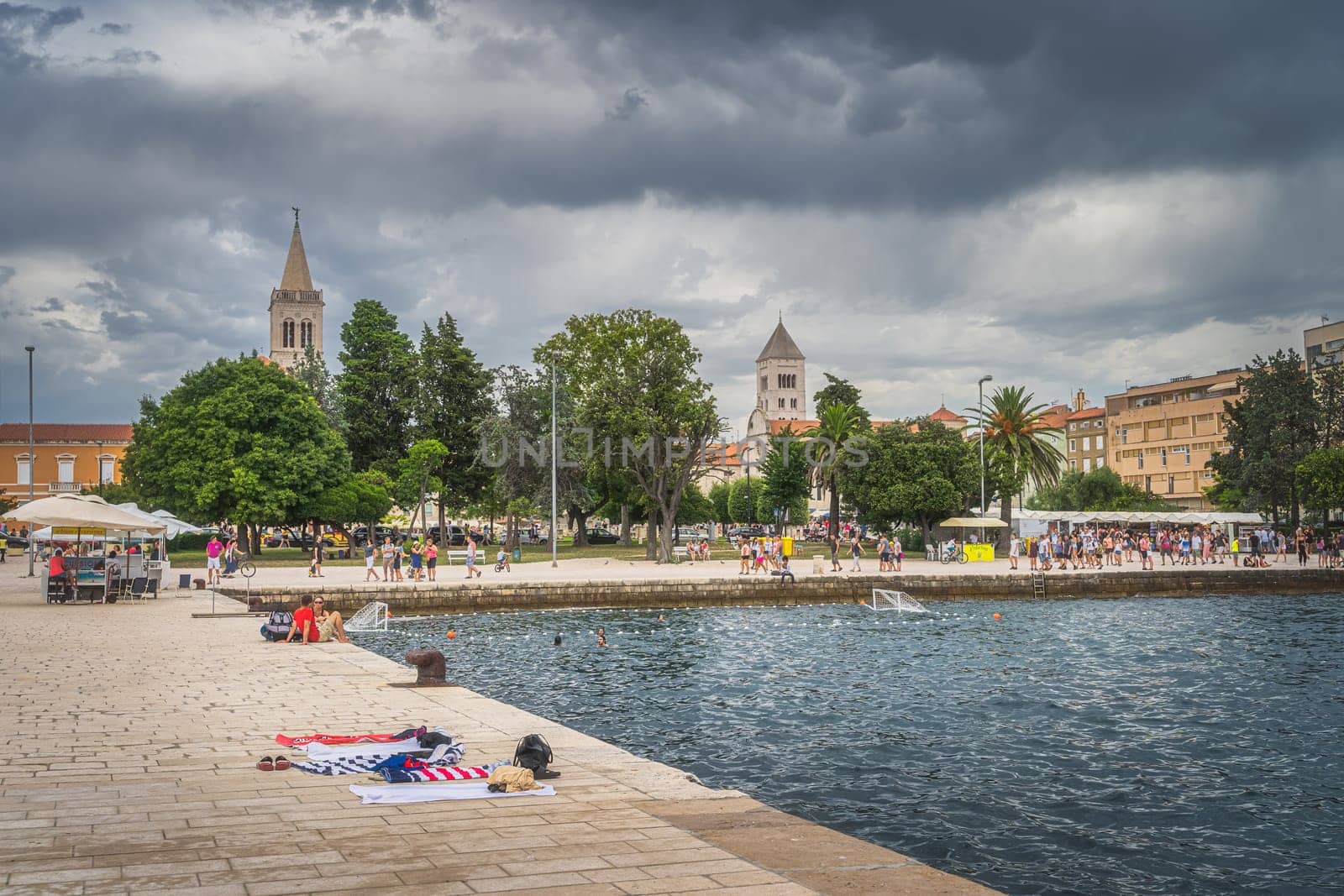 Zadar, Croatia, July 2019 Crowds of tourists walking and relaxing on the Coast of King Petar Kresimir IV. People playing water polo in Adriatic Sea