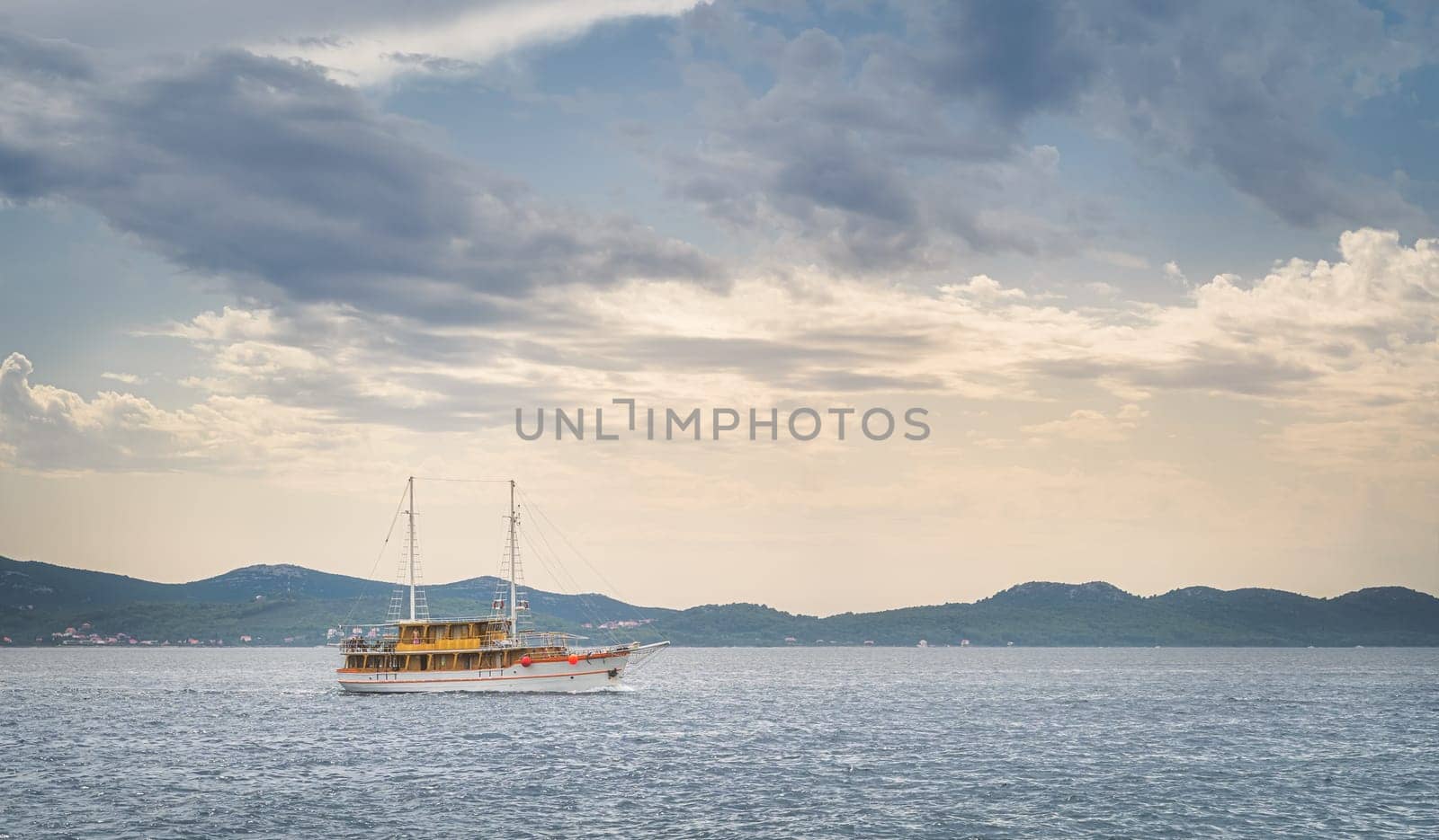 Sailboat or yacht sailing on Adriatic Sea at sunset. Coastline with mountain range seen from Zadar bay, Croatia