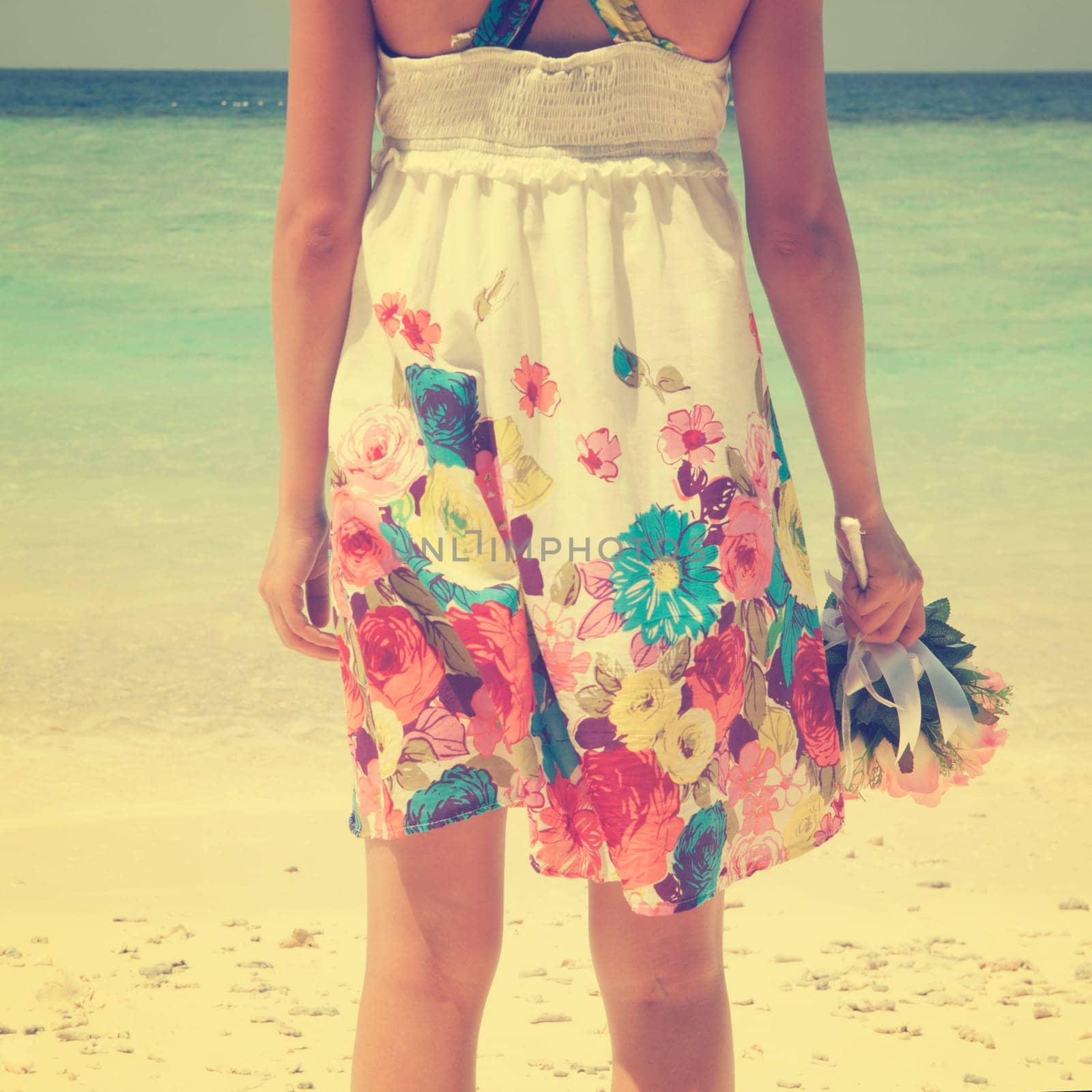 Rear view single girl standing alone at beach, hand holding flower bouquet in vintage toned.