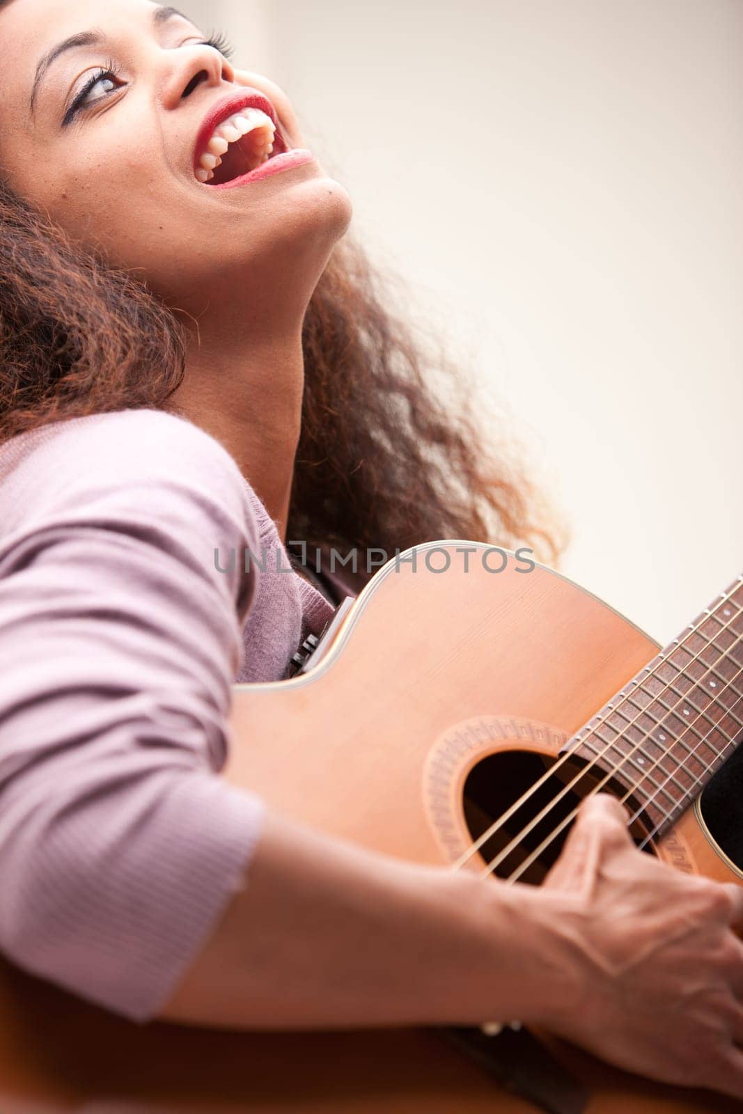 afroamerican woman singing and playing guitar on her sofa in her living room
