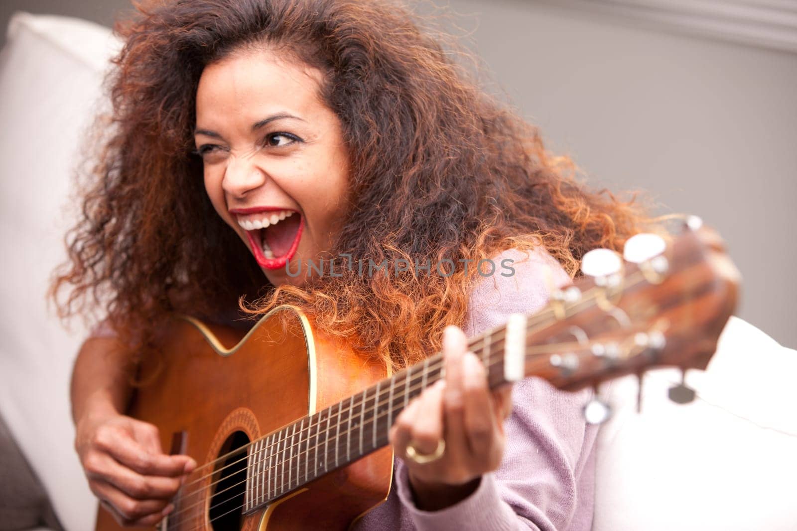 afroamerican woman singing and playing guitar on her sofa in her living room