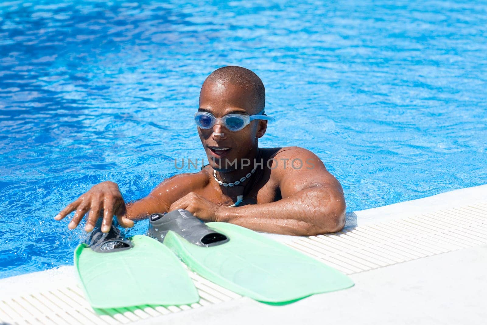 Mid adult man drying his flippers at the ledge of a swimming pool