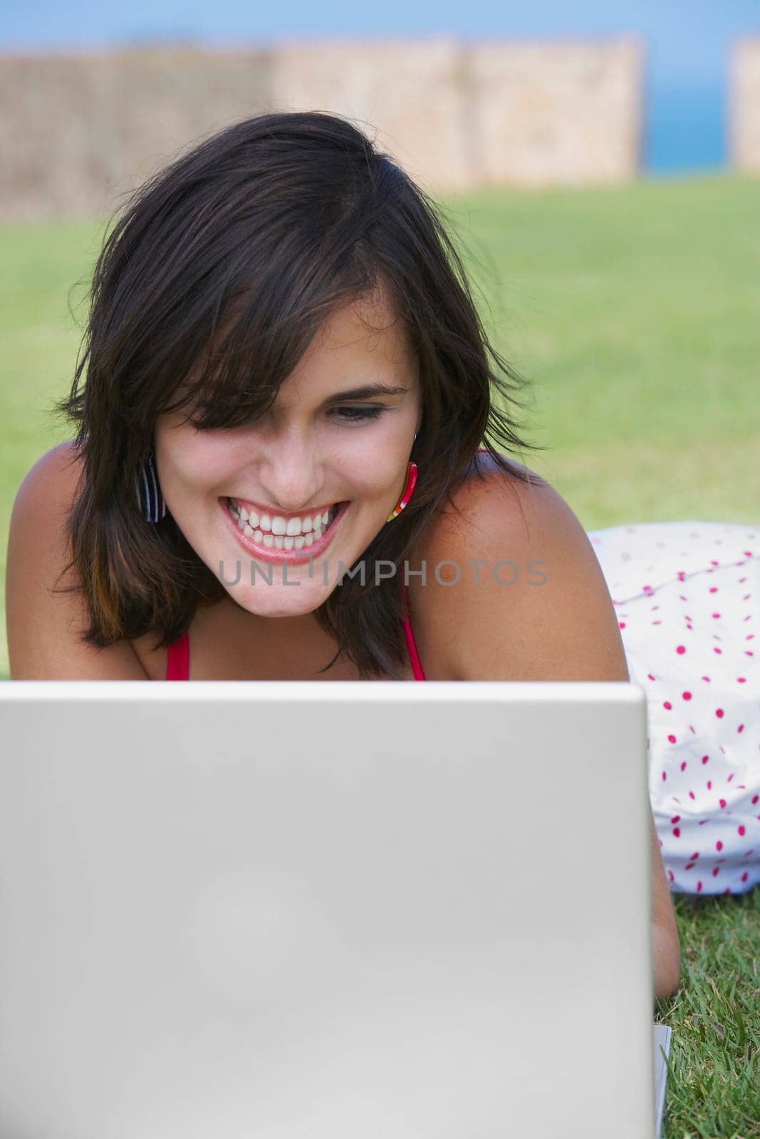 Close-up of a young woman lying in a lawn in front of a laptop
