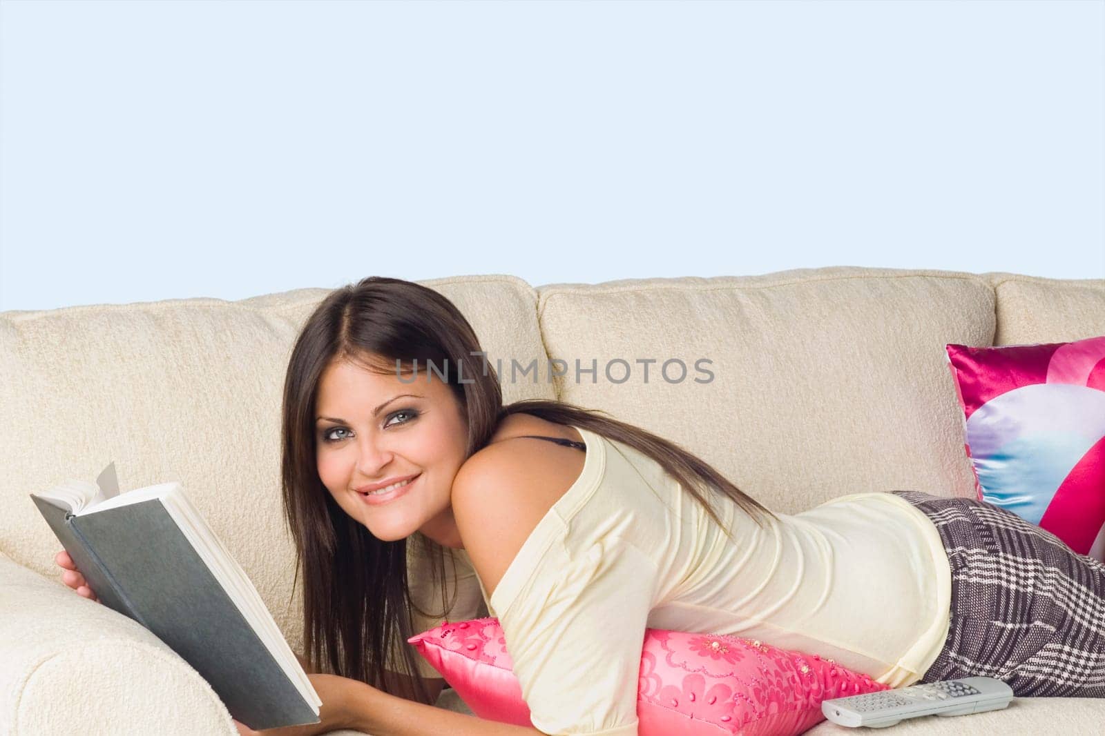 Portrait of a young woman lying on a couch and holding a book