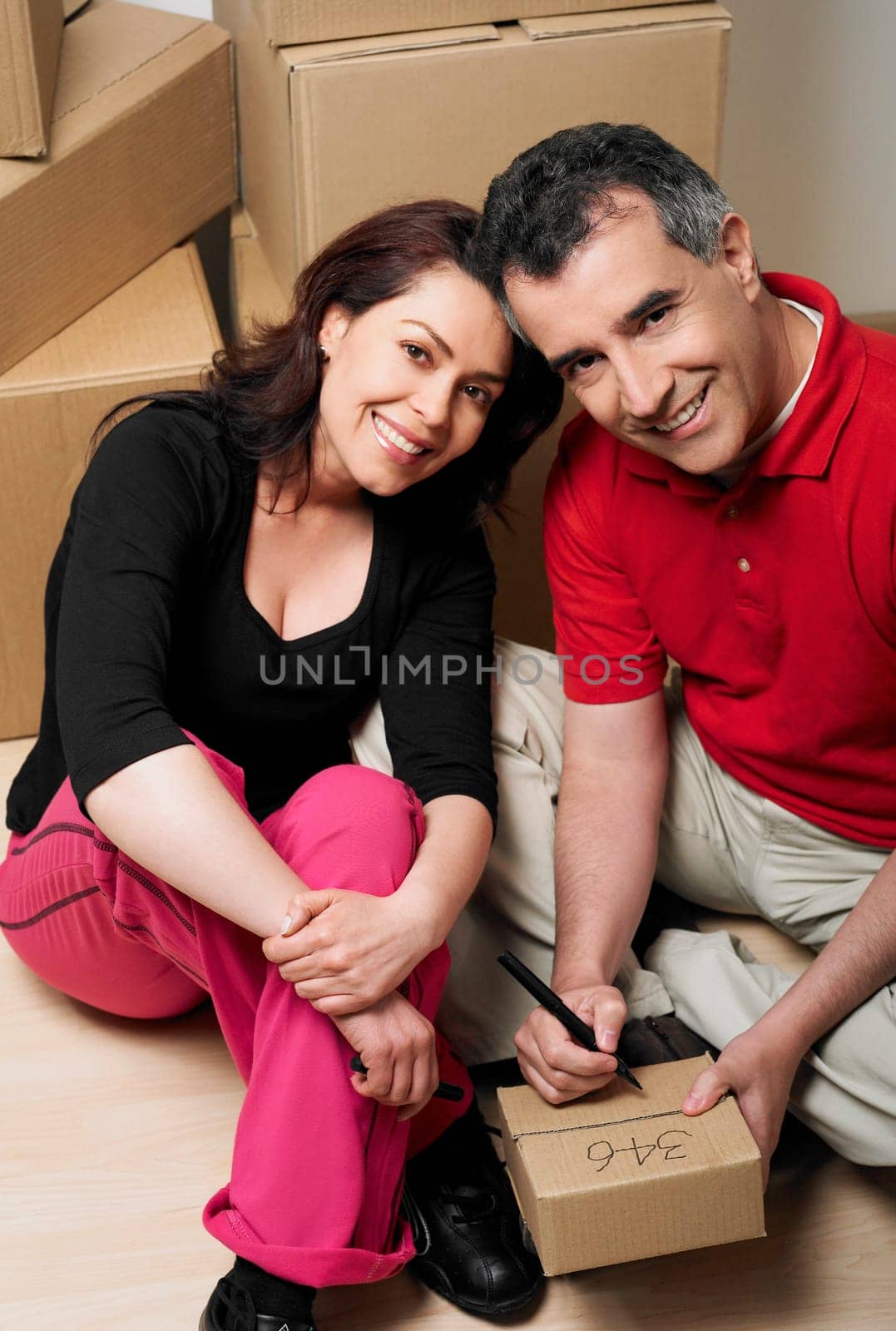 Portrait of a mid adult man writing on a cardboard box with a mid adult woman sitting beside him
