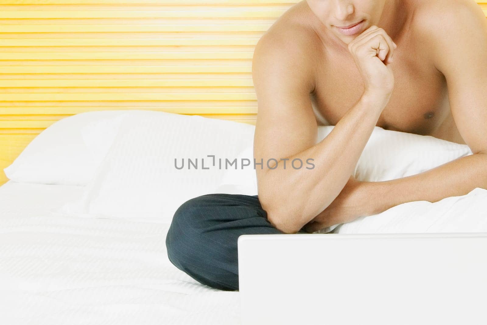 Close-up of a young man sitting on the bed in front of a laptop