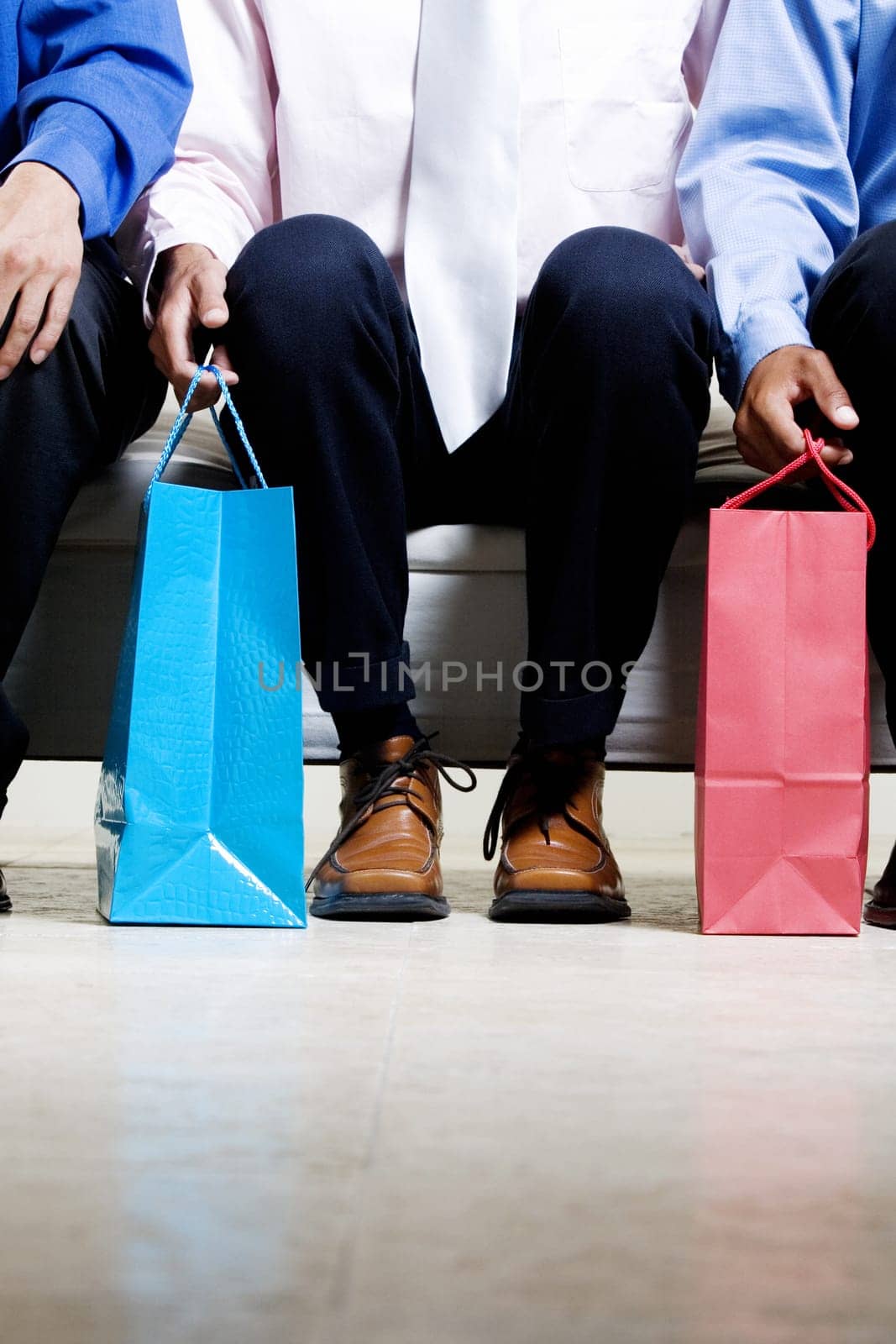 Low section view of three people sitting on a couch holding shopping bags