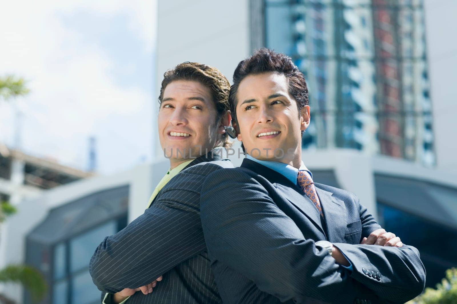 Two businessmen standing back to back and smiling