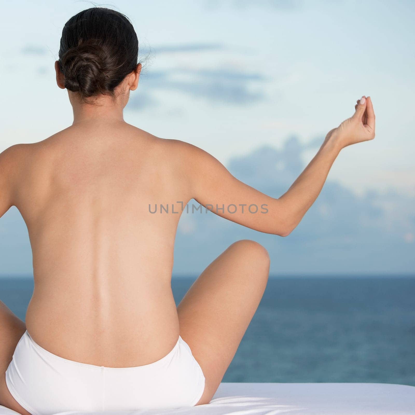 Rear view of a young woman sitting in a lotus position with her arms outstretched