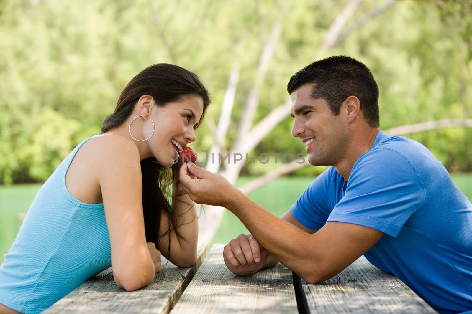Side profile of a mid adult man feeding a young woman a strawberry