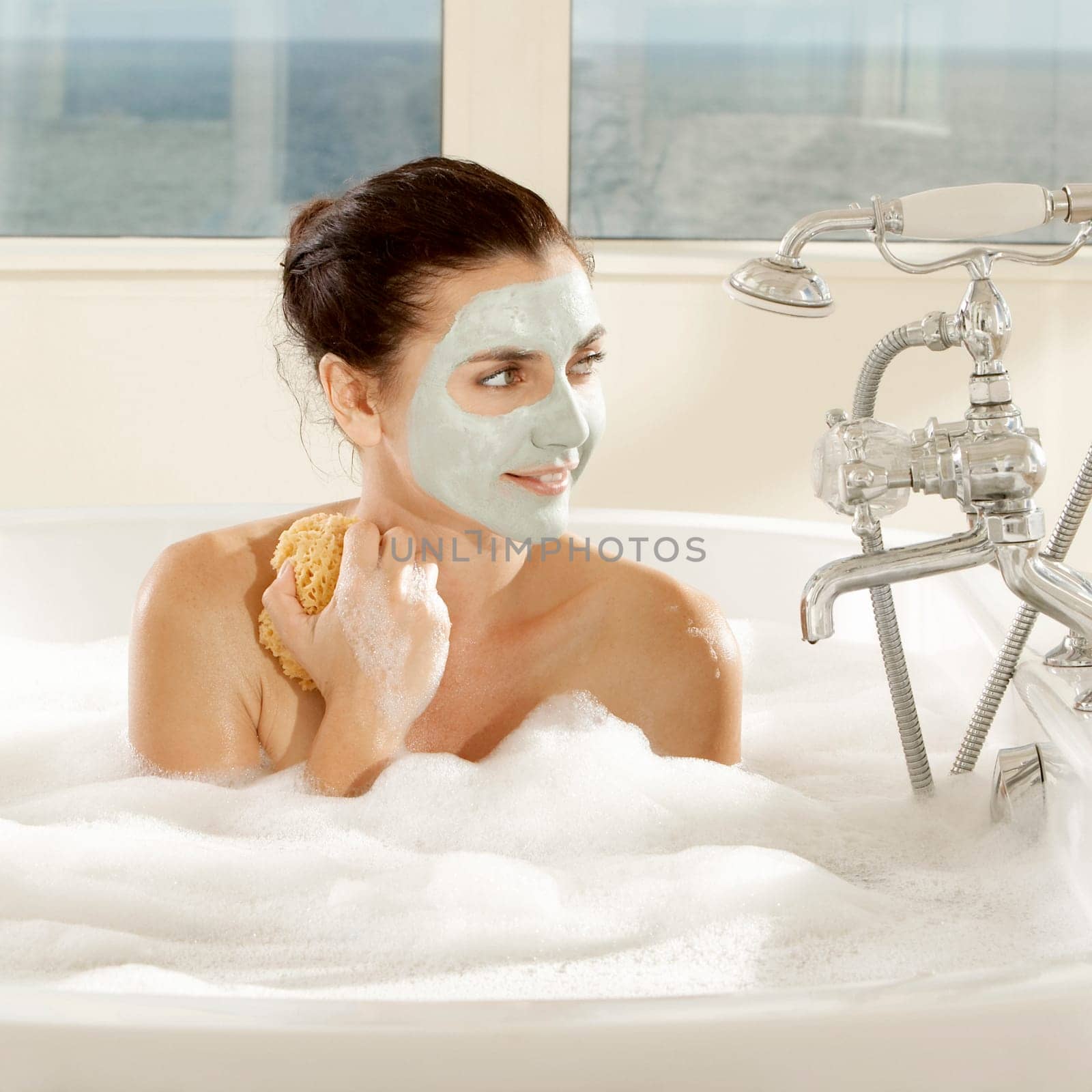 Close-up of a young woman with a facial mask holding a bath sponge