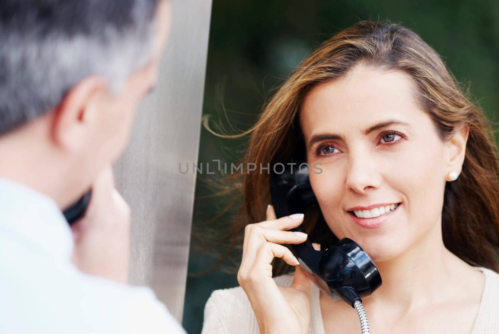 Mid adult woman talking on a pay phone with a mid adult man in front of her