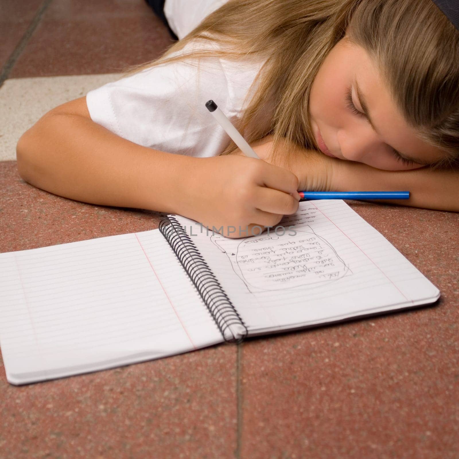 Schoolgirl lying on the floor and writing in a spiral notebook