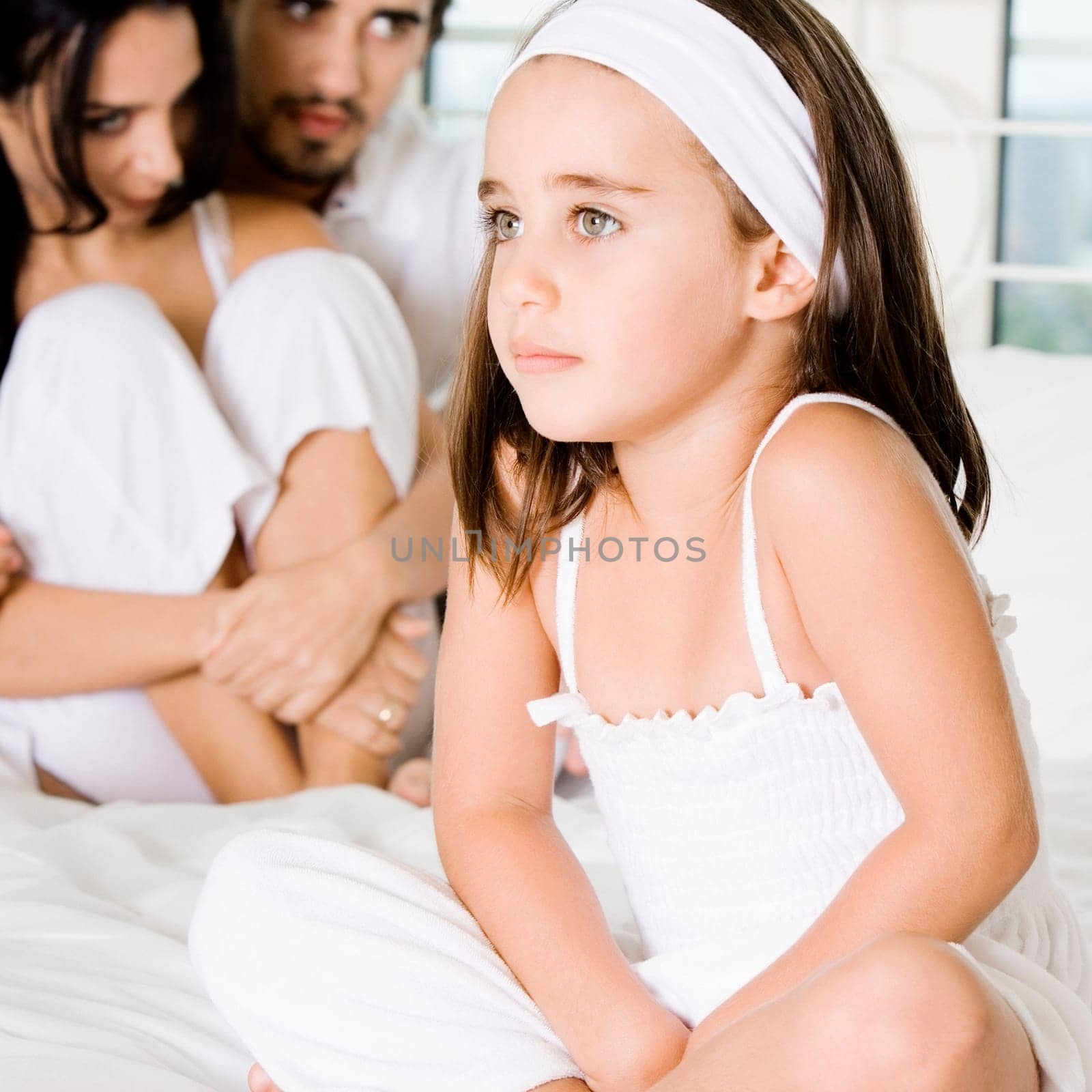 Close-up of a girl sitting on the bed with her parents behind her