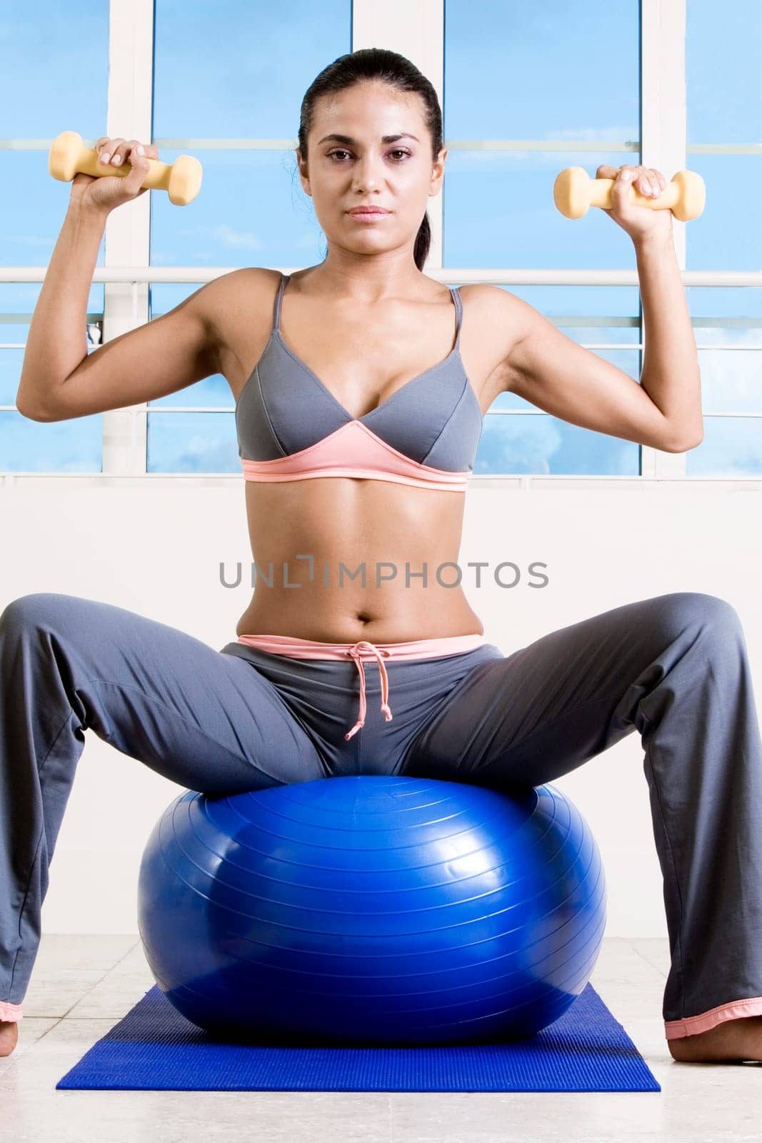 Portrait of a young woman exercising with dumbbells on a fitness ball