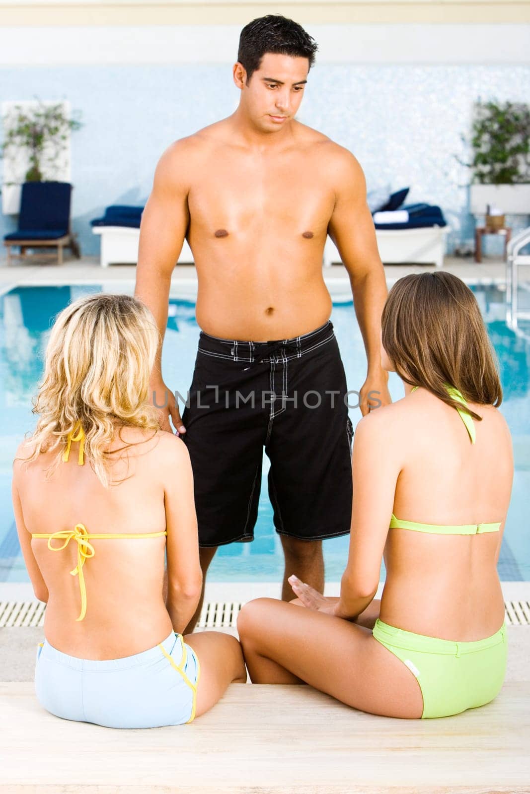 Mid adult man standing in front of two young women at the poolside