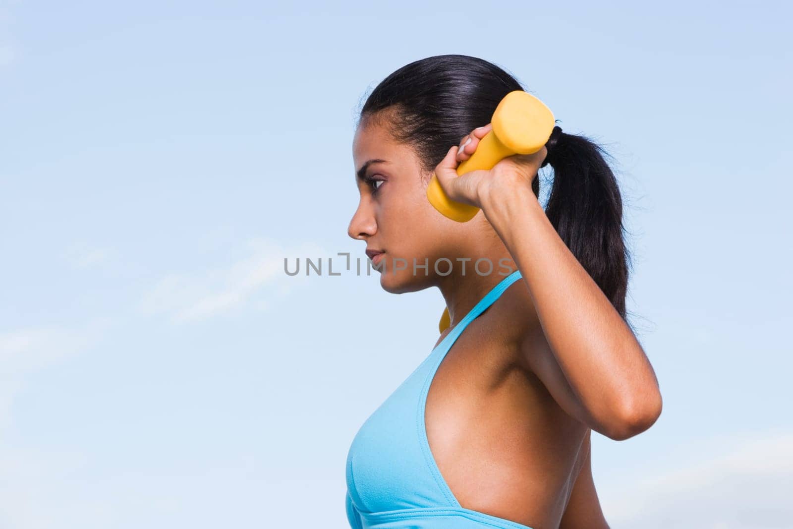 Side profile of a young woman exercising with dumbbells