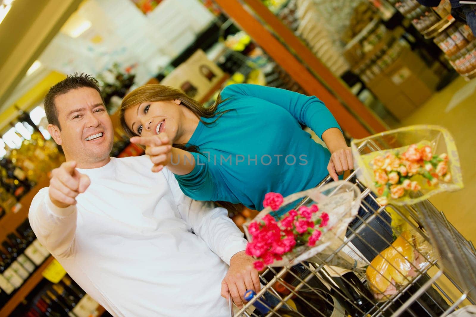 Young woman and a mid adult man standing in a supermarket and pointing forwards
