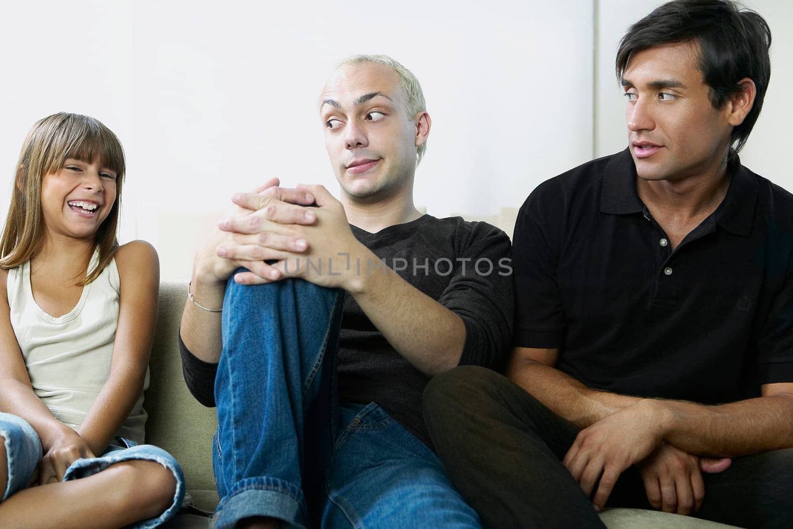 Two young men sitting on a couch and looking at a girl laughing