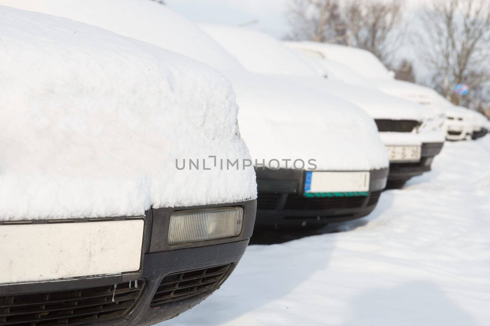 Snow covered cars parked in a row next to each other. Cars on the street in cold winter.