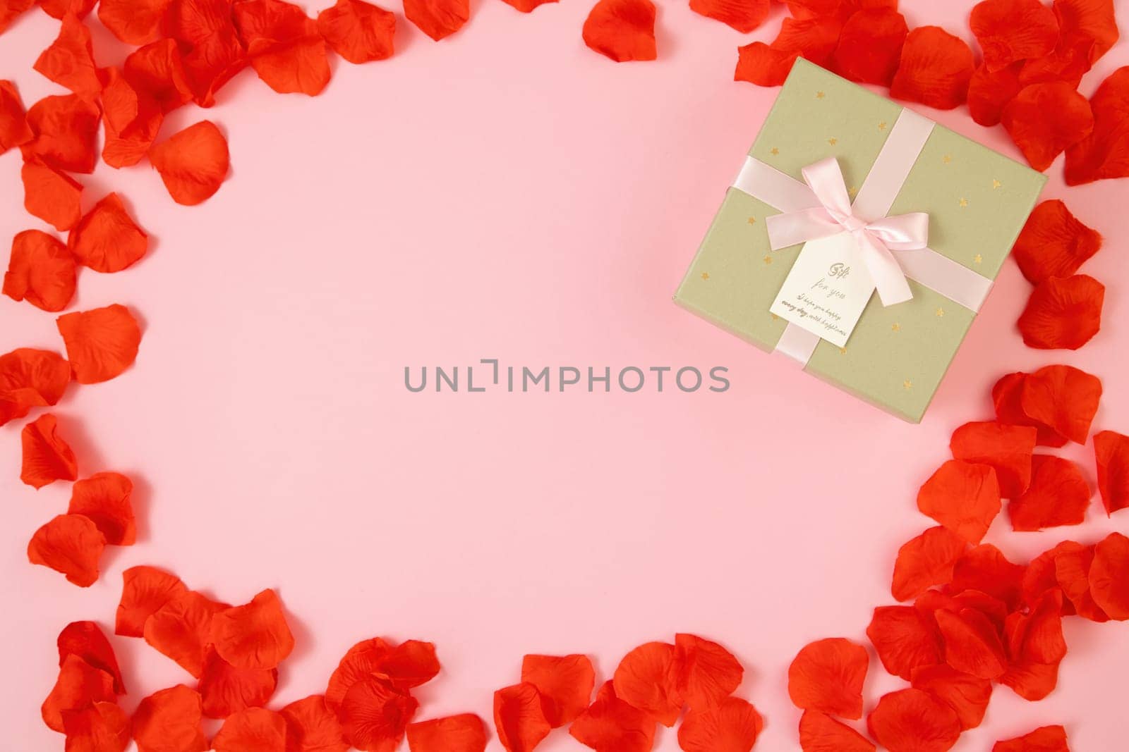 Pink background with present and rose leaves around with copy space. Golden box with ribbon on backdrop. Gift lying on table with space for text.