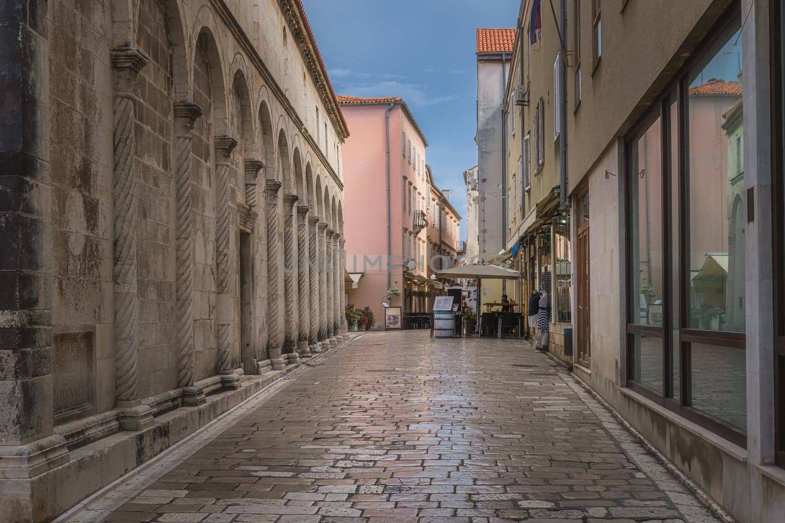 Tourists dining in outdoor restaurants in narrow streets of the old town district, surrounded by ancient Romanesque architecture, Zadar, Croatia