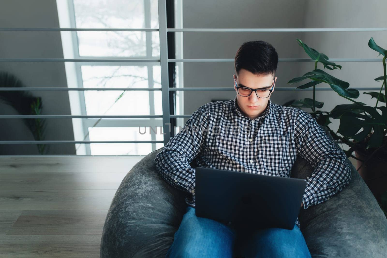 Man using laptop, wearing glasses, cushioned furniture. Blurred background. High quality photo