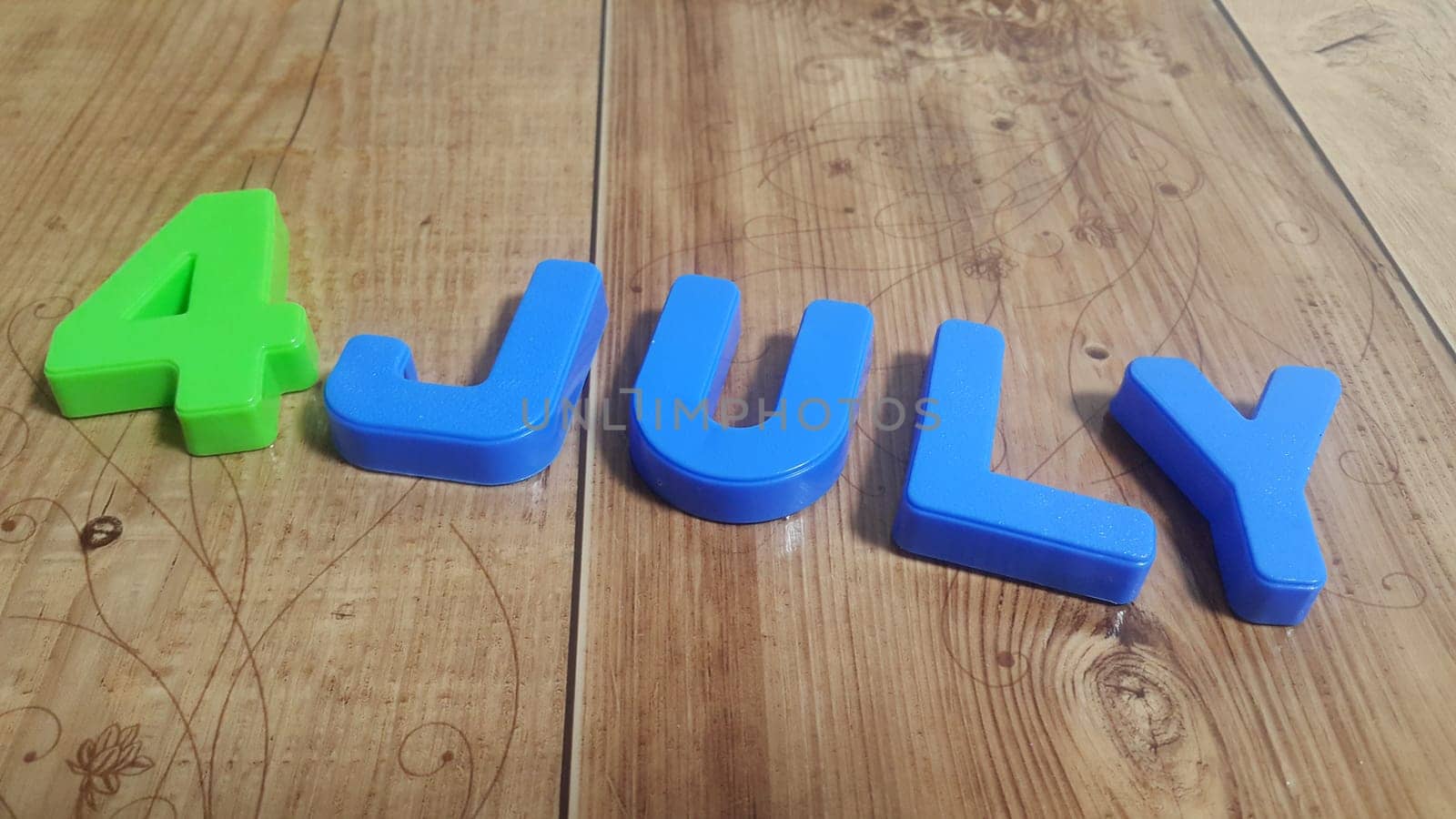 Plastic colored alphabets making words 4 july are placed on a wooden floor. These plastic letters can be used for teaching kids.